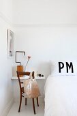 White wall-mounted shelf used as bedside table and vintage chair with bag on backrest in period apartment