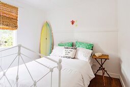 Weisses Metallbett mit Kissen, Nachttisch und Surfbrett im Schlafzimmer