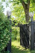 Open garden gate with artworks on posts and view into summery garden