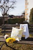 Cushion cover and tea towel embroidered with roses next to daffodils on garden bench