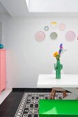 Weisser Tisch mit Vase in Kaktusform und grüne Sitzbank im Esszimmer, pastellfarbene Dekoteller an der Wand