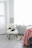 Rattanstuhl mit weißem Schaffell und Katze neben rosa Wolldecke und Zeitschriften