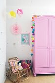Pink wardrobe and cane rocking chair in pretty, girl's bedroom