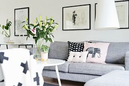 Scatter cushions on pale grey couch and vase of lilies on round table