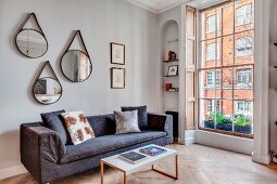 Three mirrors above grey sofa in renovated townhouse apartment