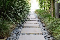 Garden path with stone slabs and pebbles between green plants