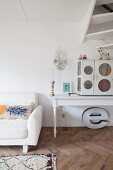 Polstersofa neben weißem Holztisch mit Vintage Schränkchen unter Treppe in Wohnraum mit Fischgrätparkett