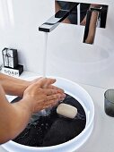 Händewaschen über weißem Kunststoffwaschbecken mit Platte in schwarzer Schieferoptik und Designer-Wandarmatur