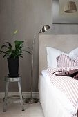 Plant on metal stool used as bedside table against grey wall