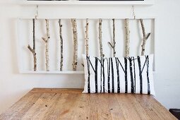 Scatter cushion with pattern of branches on wooden table below 3D artwork made from birch branches