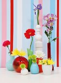 Bunte Vasensammlung mit verschiedenen Blüten dekoriert vor aufgemalten Wandstreifen