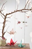 Various origami cranes hung from branch as mobile and on table