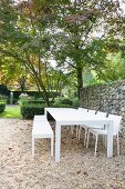 White outdoor furniture on gravel terrace with gabion wall in garden