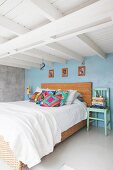 Double bed with rattan frame and vintage wooden chair below white wood-beamed ceiling