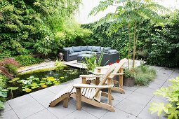 Wooden lounger on terrace next to pond and climber-covered screen wall