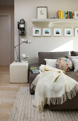 Blanket and scatter cushions on sofa below gallery of photos and floating shelf next to retro, wall-mounted telephone