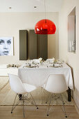 Dining table and white shell chairs below transparent red lampshade