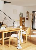 Holztisch mit Schreibutensilien und Holzstühle vor filigranem Treppengeländer und Garderobenbaum