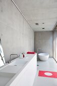 Minimalistisches Designerbad in Betonhaus mit weißer, freistehender Badewanne und rotem Farbakzent