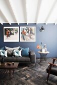 Loungebereich mit Couch, Tisch und grossformatigen Fotos an blau-grauer Wand