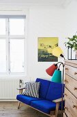Blue-upholstered couch next to retro standard lamp and chest of drawers