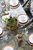 Table elegantly set with white china on wooden chargers and plant arrangement
