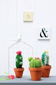 Crocheted cacti in terracotta pots in front of ornamental wire house