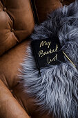 Book with bucket list on a leather sofa with sheepskin