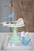Hand-made wire birdcage and bird figurine, cake stand, sheet music and bird whistles