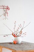 Branches of crab apples in vase and pear on wooden table in front of candy cane hung from coat rack