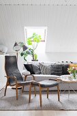Sofa and armchair with footstool in shades of grey below sloping ceiling in Scandinavian living room