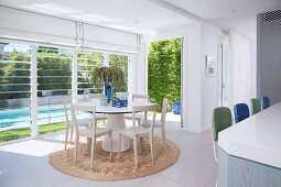 Light-flooded living room with a round dining table and a view of the pool in the garden through blinds
