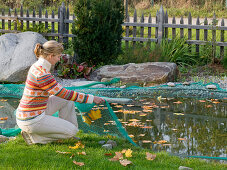 Junge Frau deckt Teich zum Schutz vor Laub mit Netz ab