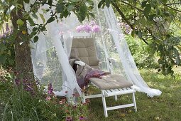Lounger with mosquito net in the meadow under the apple tree