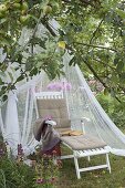 Lounger with mosquito net in the meadow under apple tree