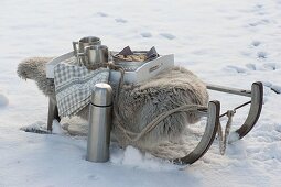 Schlitten mit Lammfell und Thermoskanne im Schnee