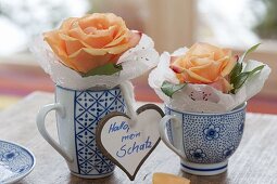 Einzelne Blüten von Rosa (Rosen) mit Tortenspitze in Tassen