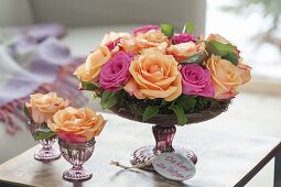 Gesteck aus Rosa (Rosen) mit Moos in flacher Schale mit Fuß und Gläschen