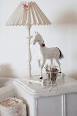 Table lamp and wooden horse on wheels on white cabinet