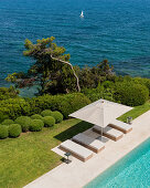 View down onto pool with loungers and manicured garden next to the sea