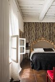 Opulent bed against patterned wallpaper in bedroom with wood-beamed ceiing