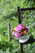 Hydrangeas and roses in vintage-style colander hung from fence