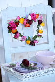 Colourful heart-shaped wreath of flowers hung on backrest of vintage chair