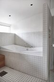 Bathtub in white-tiled bathroom with glass door screening shower