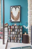 Large framed necklace above bookcase on blue wall