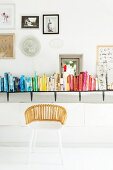 Weißer Korbstuhl vor farblich sortierten Büchern auf Wandboard