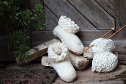 weiße, handgefertigte Filzpantoffeln und Strickzeug vor rustikaler Holztür