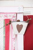 Tin bucket with love-heart motif and branch of pine cones hung from window frame with strips of fabric