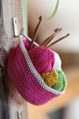 Pink crocheted basket hung from hook on wooden board