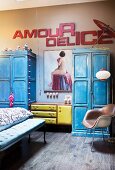 Schlafzimmer mit blauen Vintage Holzschränken, gepolstertem Retro-Sideboard unter Aktgemälde und Deko-Buchstaben an beigefarbener Wand
